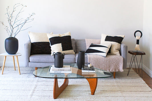 A couch with black and white throw pillows and black resin vases on a coffee table.