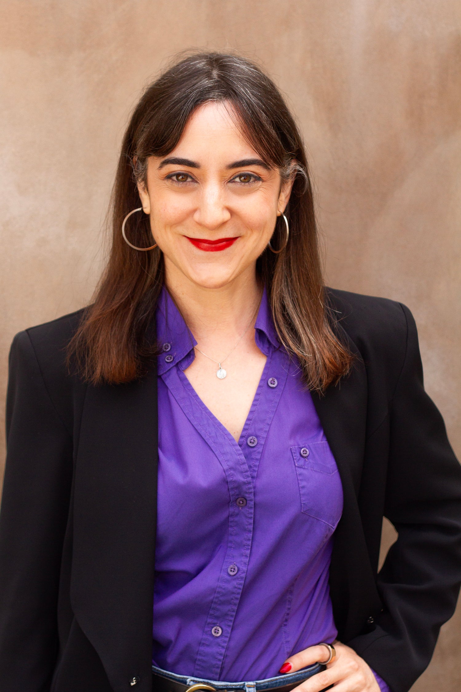 Woman wearing a purple shirt and black blazer against a beige background